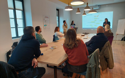 Atelier collaboratif chez Optesys Conseil : des participants échangent autour d’une présentation projetée, dans une salle lumineuse au cadre convivial et moderne.
